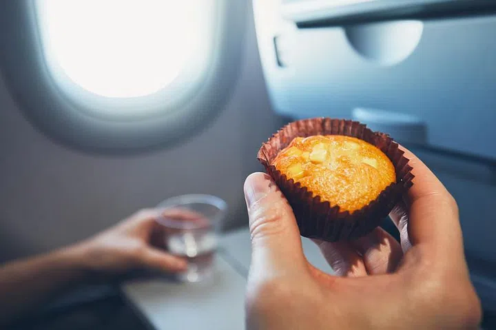 Comfortable traveling by airplane. Passenger is holding muffin and drinking glass with water during the flight.