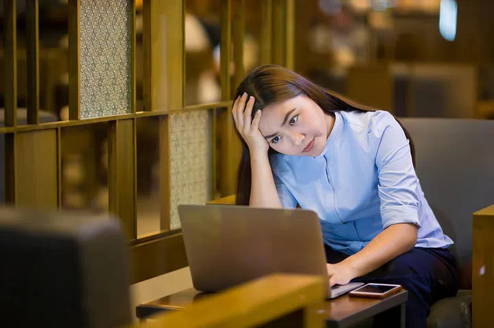 Woman using laptop in cafe at night time and she feel worried