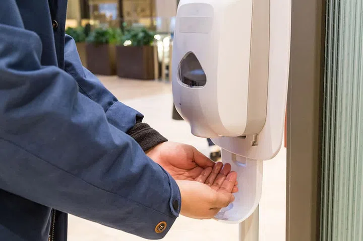 Person cleaning hand with anti-bacterial hand disinfectant sanitizer dispenser in public mall in Japan