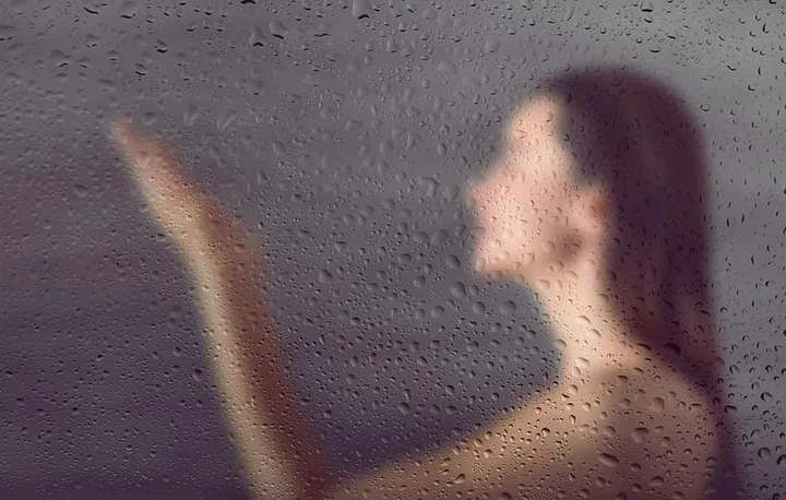 View through steamy glass on young woman in shower