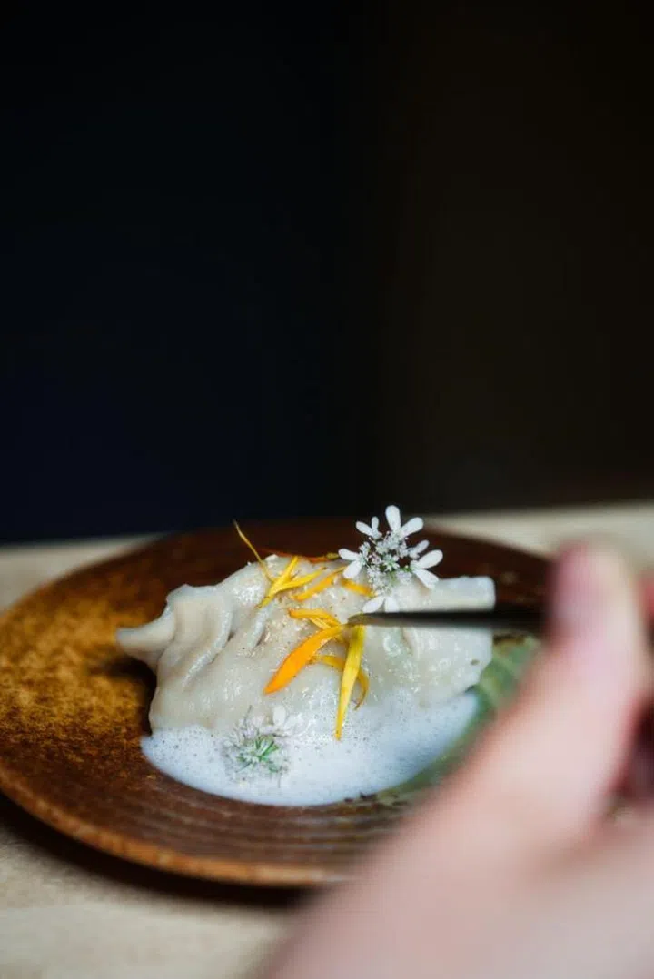 Dumpling of blue mussels and fermented potato, tom kha foam with mussel jus, marigold and coriander flowers. Photo: Saga