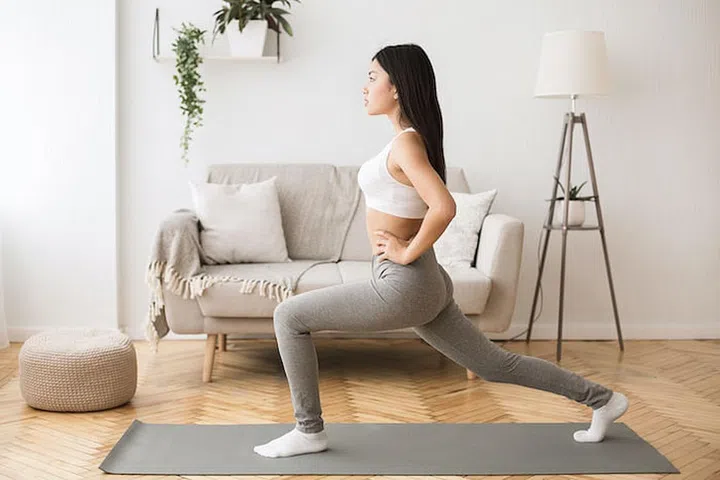 Home workout. Girl doing aerobics warming up for flexibility, leg stretching