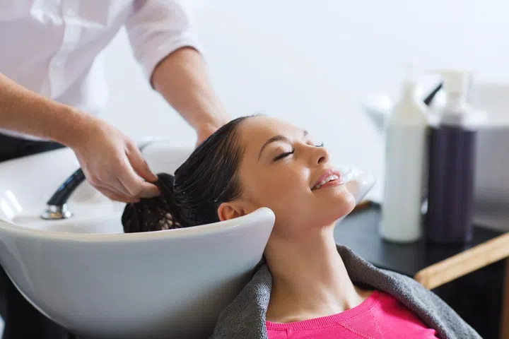beauty and people concept - happy young woman with hairdresser washing head at hair salon