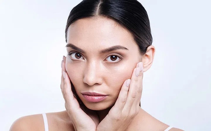 Beautiful flower. Attractive dark-haired young woman cupping her face with her hands while posing against a white background