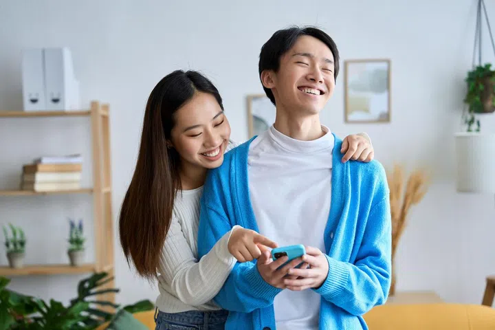 young asian couple enjoying watching funny videos on mobile phone