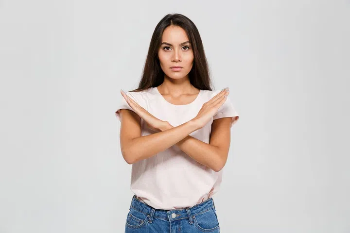 Portrait of a serious concentrated asian woman standing with crossed hands showing stop gesture isolated over white background