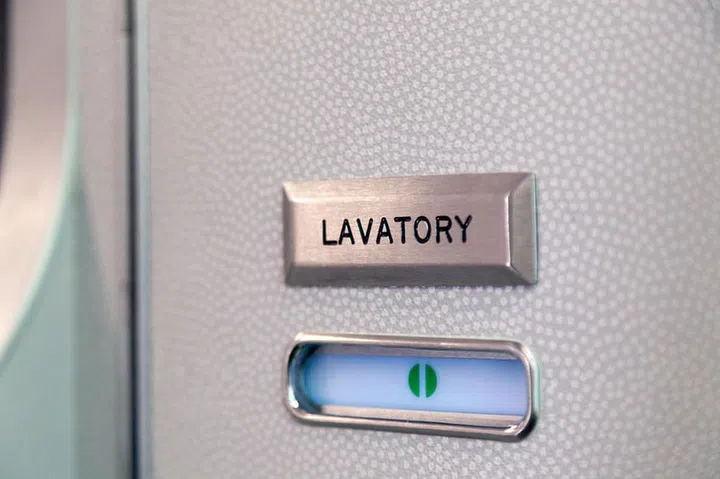 Vacant green sign, vacant symbol on an airplane lavatory door. Raised, brushed metal lavatory sign, recessed plastic vacant sign. Toilet room, wc, water closet on airplane board