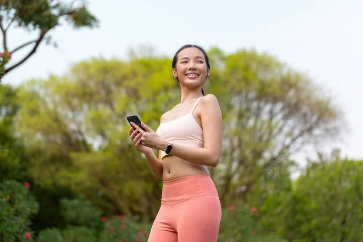 Asian Woman Using Phone While Exercising Outdoors In a Park