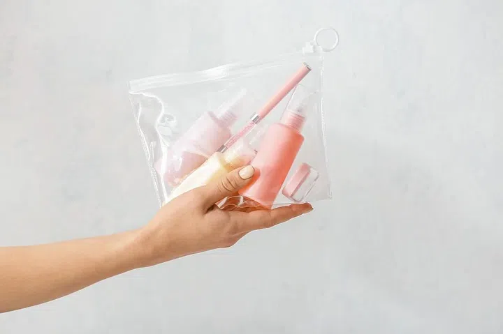 Female hand and bag with travel bottles of body care cosmetics on light background