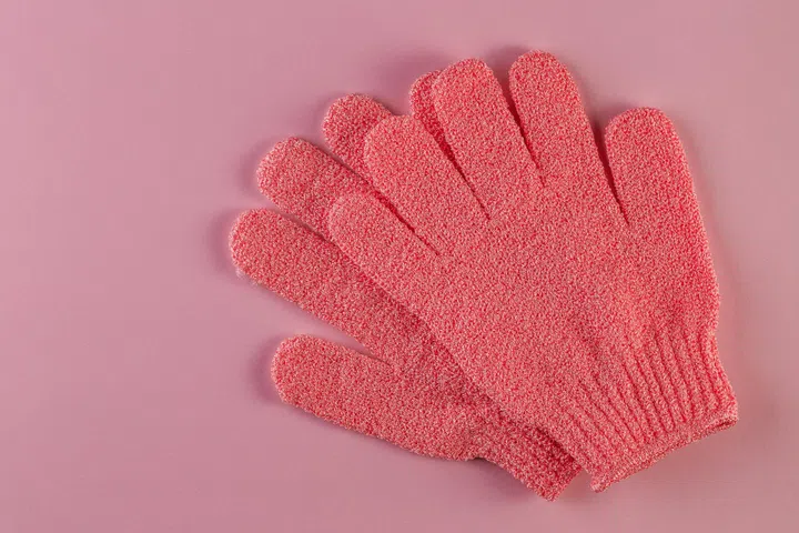 A pair of pink massage gloves for shower on pink background. Gloves for use in the shower for massage and scrub. Beauty background with cosmetic products. Beauty, health and spa concept