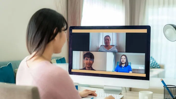 Back view of Asian business woman talking to her colleagues about plan in video conference. Multiethnic business team using computer for a online meeting in video call. Group of people smart working from home.