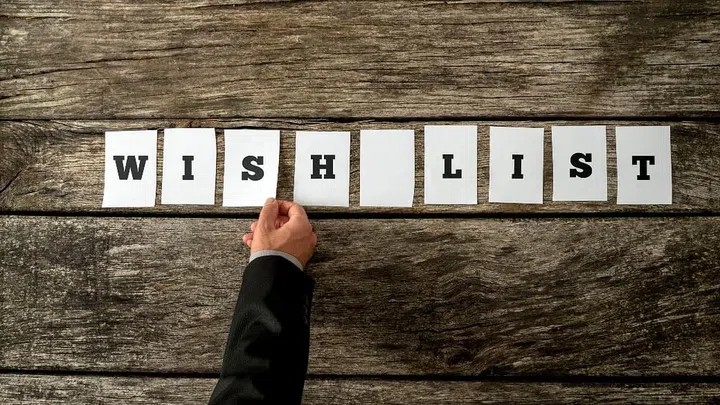 Overhead view of male hand assembling a sign WISH LIST with cards with letters on them on a textured rustic wooden background. Conceptual of personal or organizational wishes, retail and consumerism.