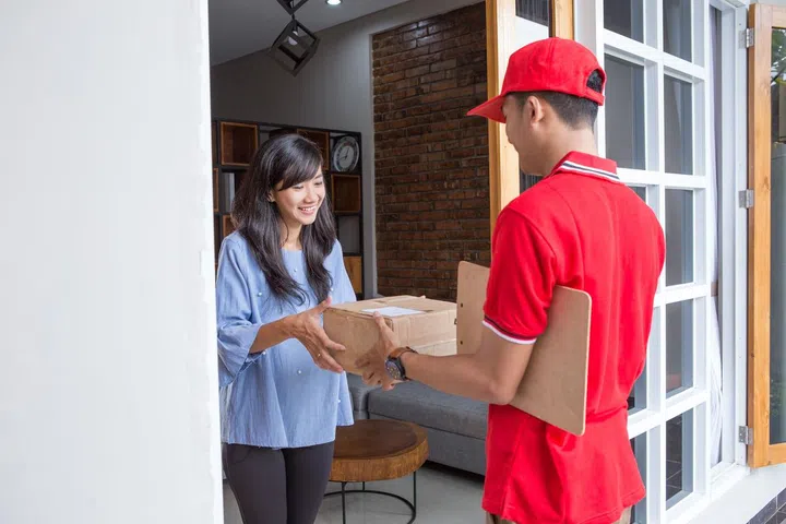 Smiling delivery man in red uniform delivering parcel box to recipient