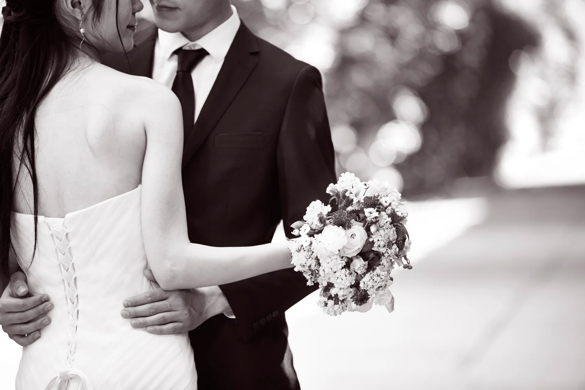 asian wedding couple hugging each other, focus on the bouquet, black and white.