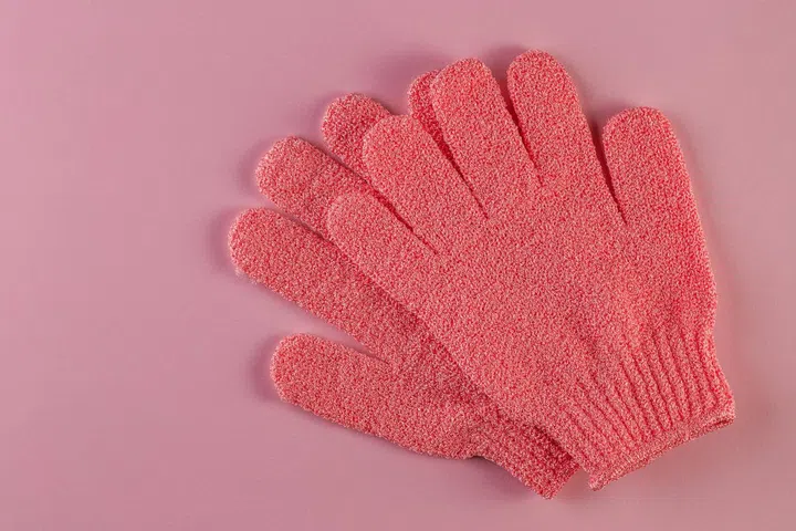 A pair of pink massage gloves for shower on pink background. Gloves for use in the shower for massage and scrub. Beauty background with cosmetic products. Beauty, health and spa concept