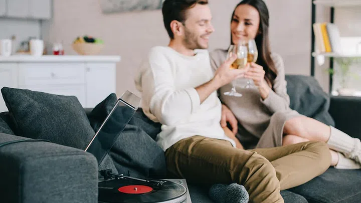 happy young couple listening music with vinyl record player and drinking wine at home