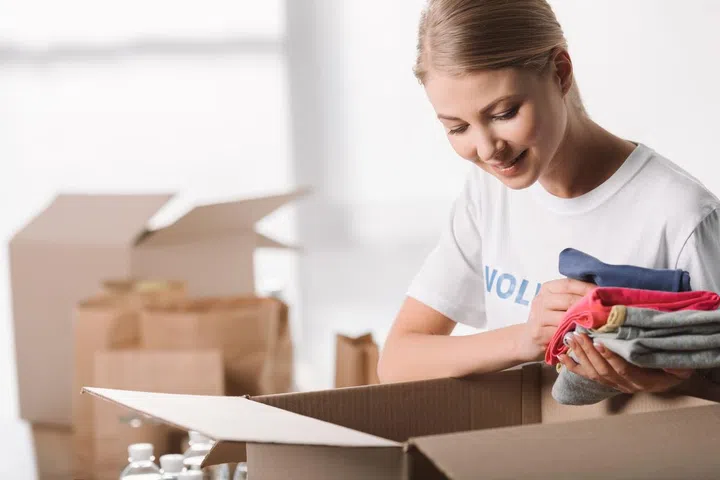 beautiful female volunteer putting clothes into box for charity