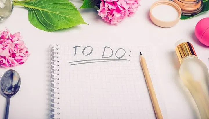 Female working place with To do list, cosmetic accessories, parfumes and wisteria flowers on the white background. Day planning. Fashion, Beauty blog concept