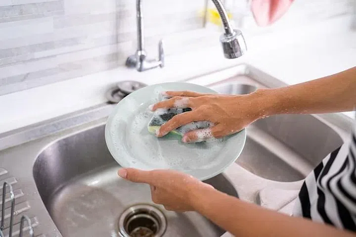 female hand gesture cleaning plate using sponge and soap in the kitchen sink