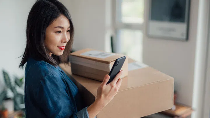 asian woman carrying boxes while looking at phone 
