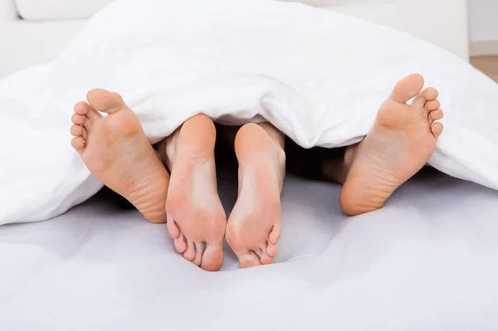 Low section of intimate couple under blanket on mattress at home
