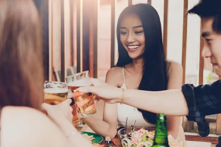 Asian people cheering beer at restaurant happy hour and laughing and talking together.