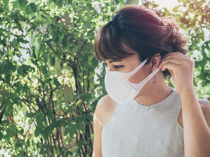 Beautiful asian woman wearing white protective N95 dust mask on green leaves background with copy space. Protection against pollution concept.