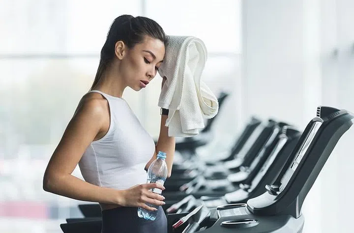 Woman tired and having rest after running on treadmill in modern gym