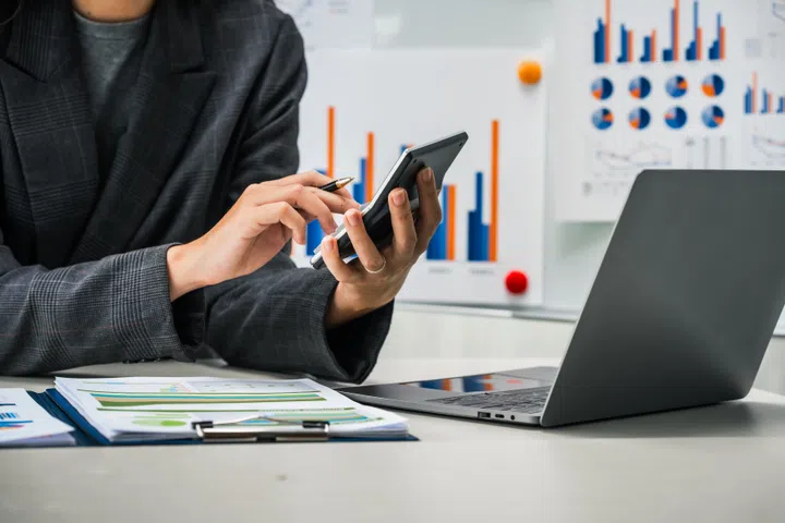 A businesswoman works diligently at her desk, reviewing financial documents and analyzing investment data. She ensures accuracy and efficiency in financial calculations and audit processes.