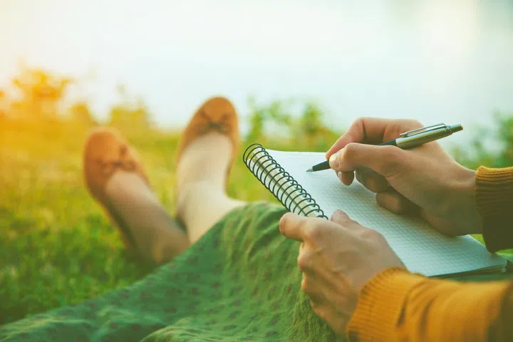 female hands with pen writing on notebook on grass outside