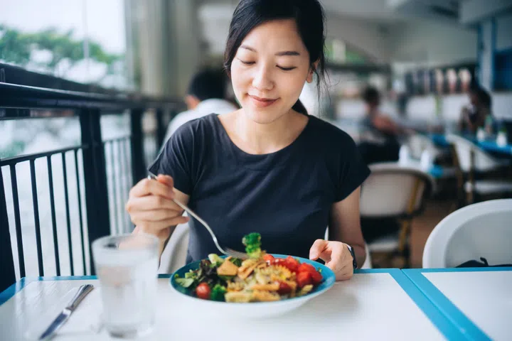 Young Asian woman enjoying a healthy meal for lunch. She is having fresh and colourful vegan salad bowl with organic greens and fruits at a vegan restaurant. Healthy eating, go green lifestyle