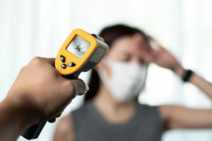 Woman  feeling sick wearing protective mask. With security's hand check at gates use digital thermometer checking temperature.