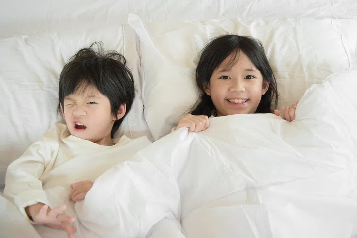 Cute asian children playing under blanket on white bed