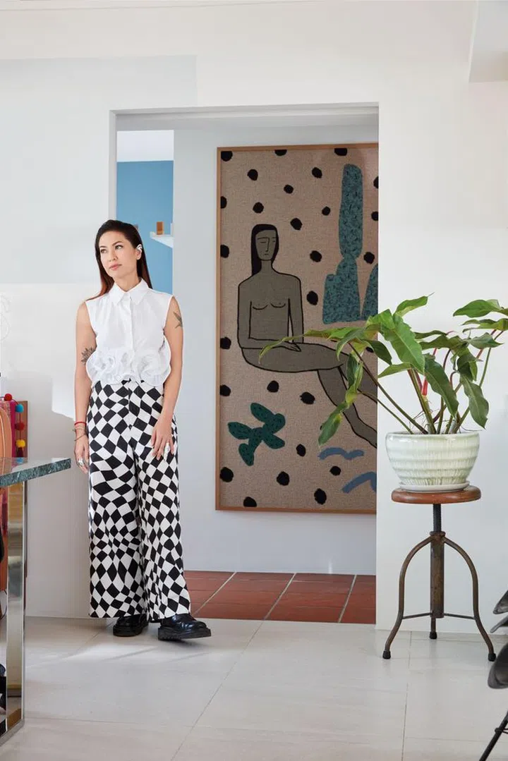Tracy Phillips dressed in her own Rochas top, Maison Margiela trousers, Toga Pulla boots, Avec earrings, and Fangophilia rings. She loves the desert and wanted to incorporate the tones into her home. Behind her hangs tapestry art from LA-based artist Lilian Martinez.Photo: Gan