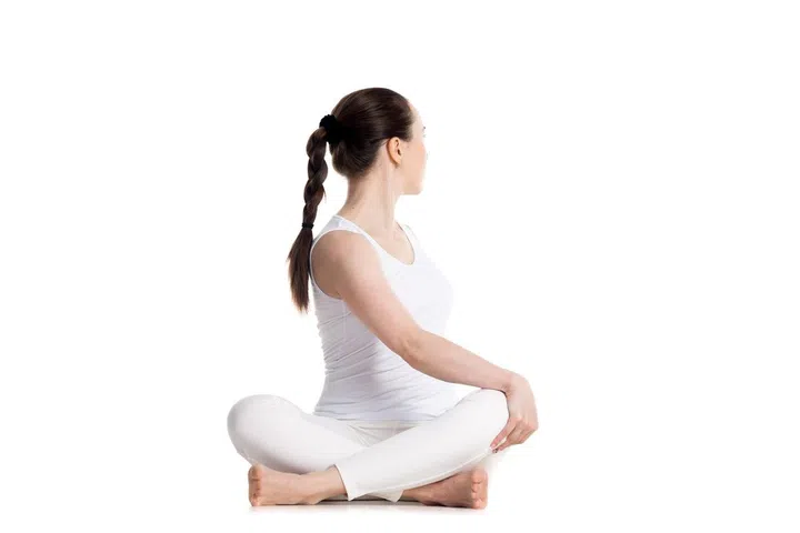 Sporty beautiful young woman in white sportswear practicing yoga, sitting cross legged in Revolved easy pose, spinal twist, parivrtta sukhasana, studio full length isolated shot, front view