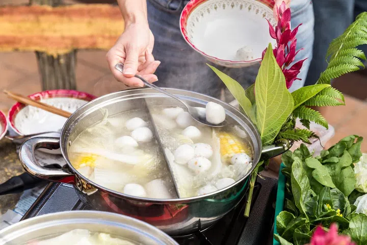 Hand adding ingredients into Asian steamboat pot dinner meal