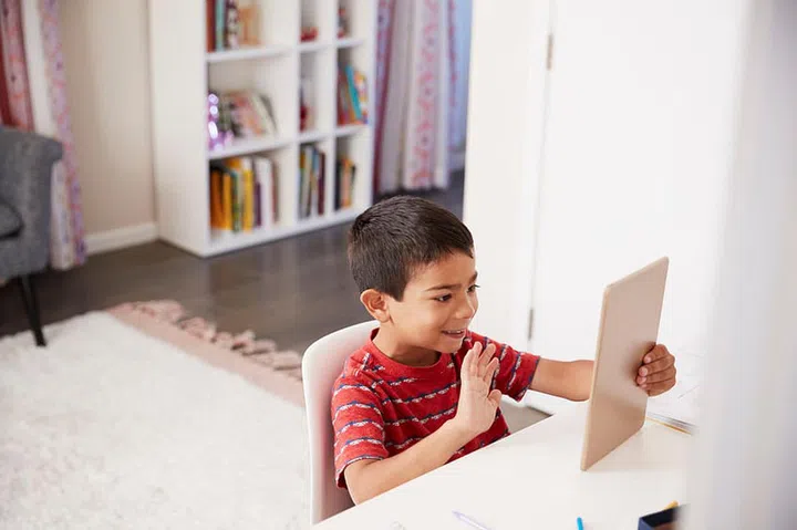 Young Boy Sitting At Desk In Bedroom Using Digital Tablet To Make Video Call