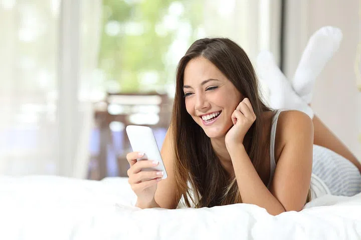 Happy girl using a mobile phone lying on the bed at home