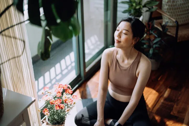 Asian woman taking a break after working out at home, sitting on exercise mat