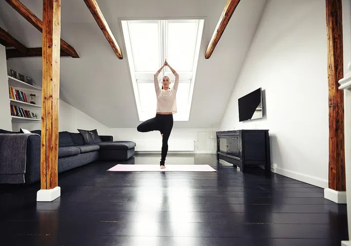 Full length image of young caucasian woman practicing yoga exercise at home. Fit young woman standing on one leg and meditating in her living room.