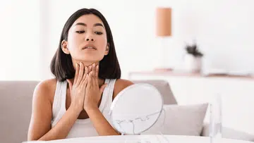 woman massaging her neck while looking into a mirror