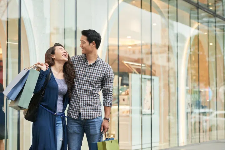 Happy young Vietnamese couple standing at large shop window