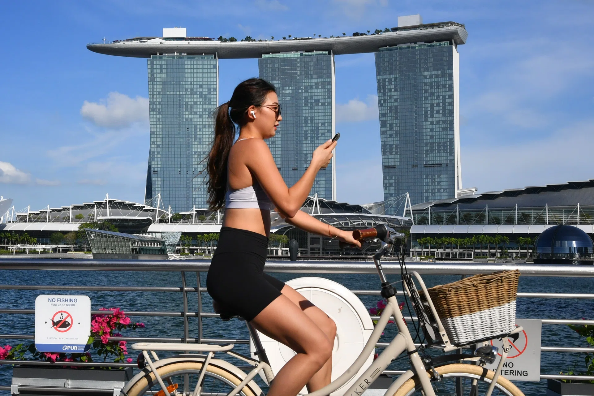 Woman cycling under the hot sun at One Fullerton near Merlion Park with Marina Bay Sands in the background on March 4, 2021.