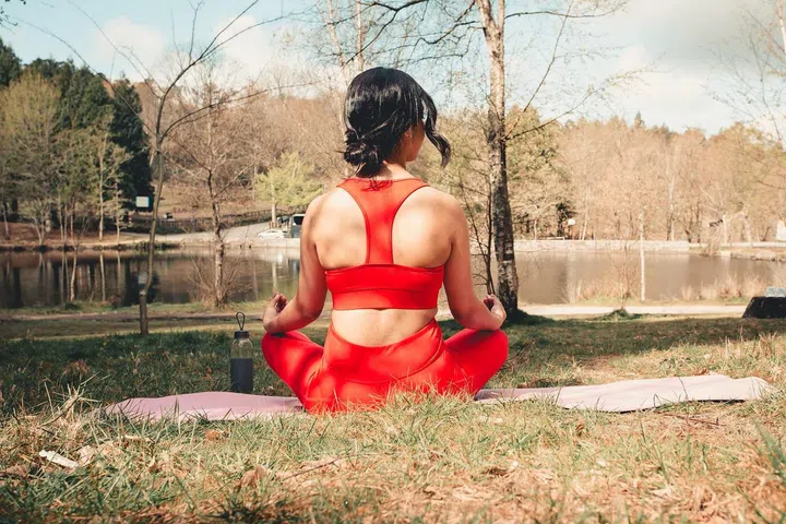 Young woman in fitness clothes doing yoga exercises over a yoga mat at the park during a sunny day