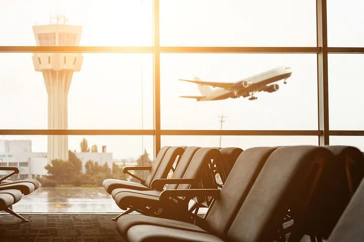 Empty chairs in the departure hall at airport , with the control tower and an airplane taking off at sunset. Travel and transportation concepts.