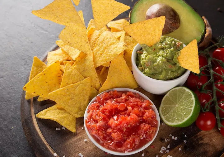 Mexican nacho chips and salsa dip on black stone background