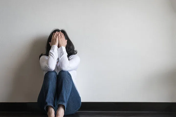 Stressful woman sitting sadly with emotional depression and anxiety on the floor in home living room with white wall