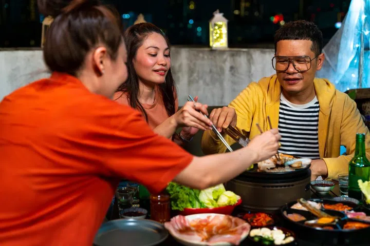 Group of Diversity Asian people friends enjoy and fun celebration meeting dinner party eating barbecue grill and drinking Korean vodka together at outdoor rooftop on summer holiday vacation at night.