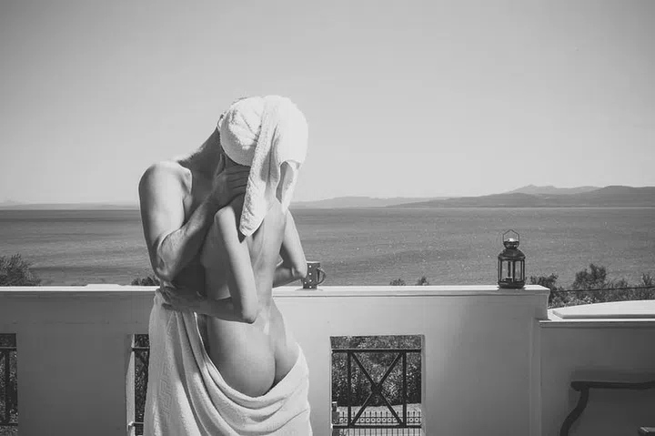 Sensual young couple making love in bedroom. Man and sexy topless lady makes love. Couple in love hugs and kissing on balcony, sea on background. Couple in towels have sex on terrace on sunny day. Romantic and honeymoon concept.