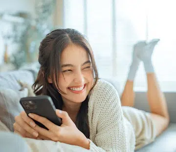 girl lying on couch using phone smiling | best online shopping sites for beauty products